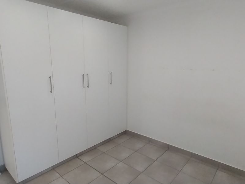 A clean, empty bedroom featuring neutral tiled flooring and ample built-in cupboard storage space.