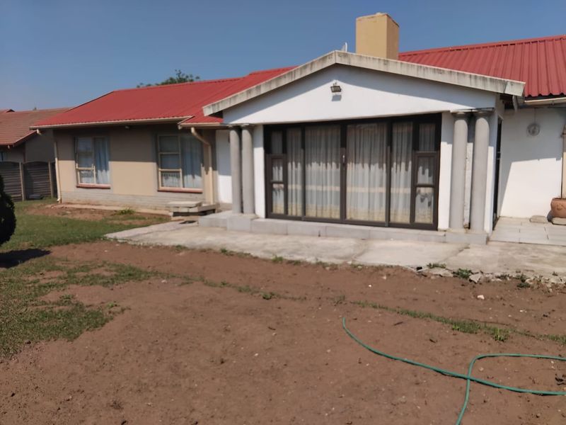 Rear view of the house featuring a red metal roof, concrete patio area, and sliding glass doors with decorative columns.