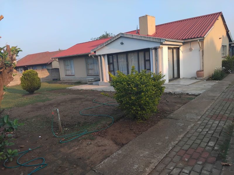 Rear view of a single-story house featuring a red corrugated metal roof, chimney, and sliding glass doors opening onto a garden area.