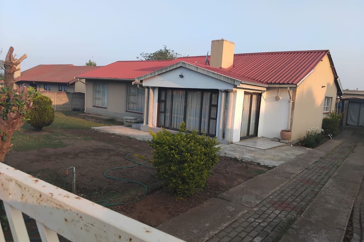 Rear view of a single-story house featuring a red corrugated metal roof, sliding glass doors, a concrete patio, and a paved driveway.