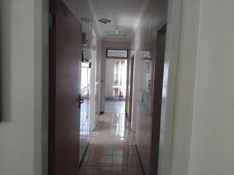 A narrow hallway featuring tiled walls and flooring, with visible ceiling damage and a central access hatch leading to other areas of the home.
