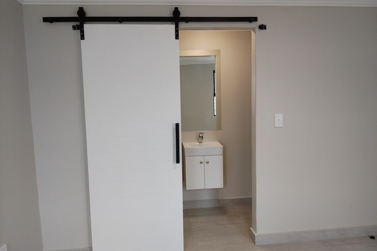 A modern bathroom featuring a wall-mounted vanity with basin and mirror, accessed via a contemporary white sliding barn door.