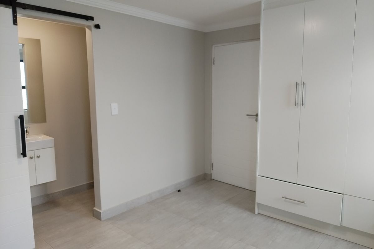 A modern, neutral bedroom featuring built-in wardrobes, tiled flooring, and an en-suite bathroom access via a sliding barn door.