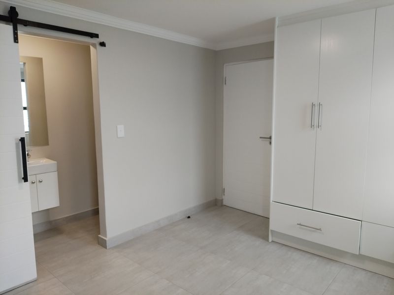 A modern, neutral bedroom featuring built-in wardrobes, tiled flooring, and an en-suite bathroom access via a sliding barn door.