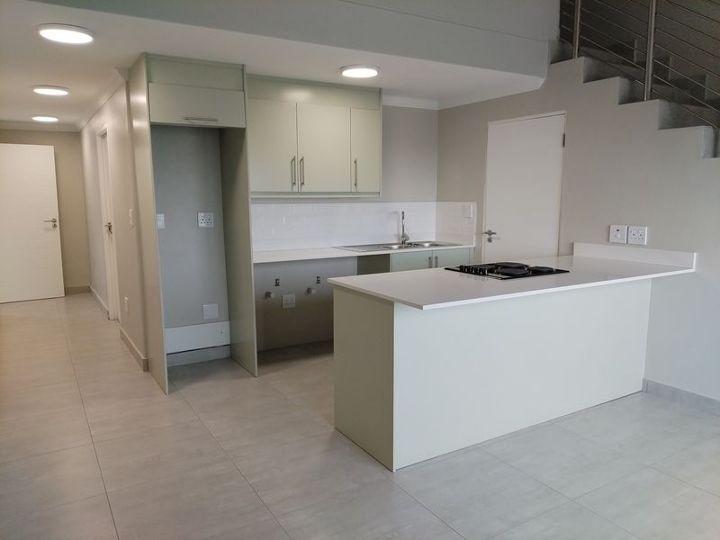 Modern open-plan kitchen featuring sleek cabinetry, stone countertops, integrated hob, and subway tile backsplash, situated beneath a staircase in a bright, contemporary apartment.