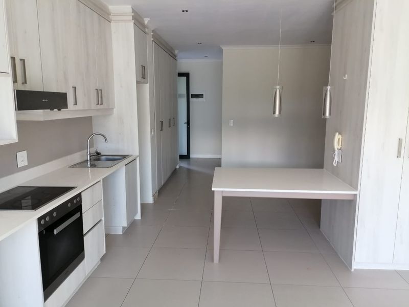 Modern open-plan kitchen featuring light wood-finish cabinetry, integrated appliances, tiled flooring, and a built-in breakfast counter, offering a clean and functional living space.