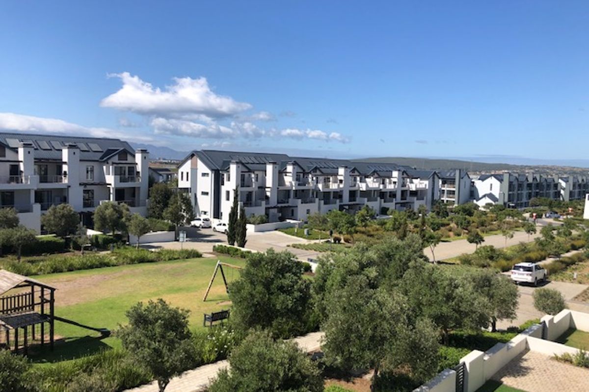 An elevated aerial view of a modern residential apartment complex featuring well-maintained communal gardens, paved pathways, and multiple building blocks with solar installations.