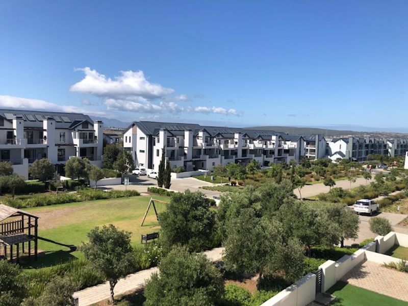 An elevated aerial view of a modern residential apartment complex featuring well-maintained communal gardens, paved pathways, and multiple building blocks with solar installations.