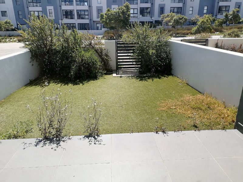 A private ground-floor garden area featuring a tiled patio, artificial lawn, and perimeter boundary walls with a gated access point.