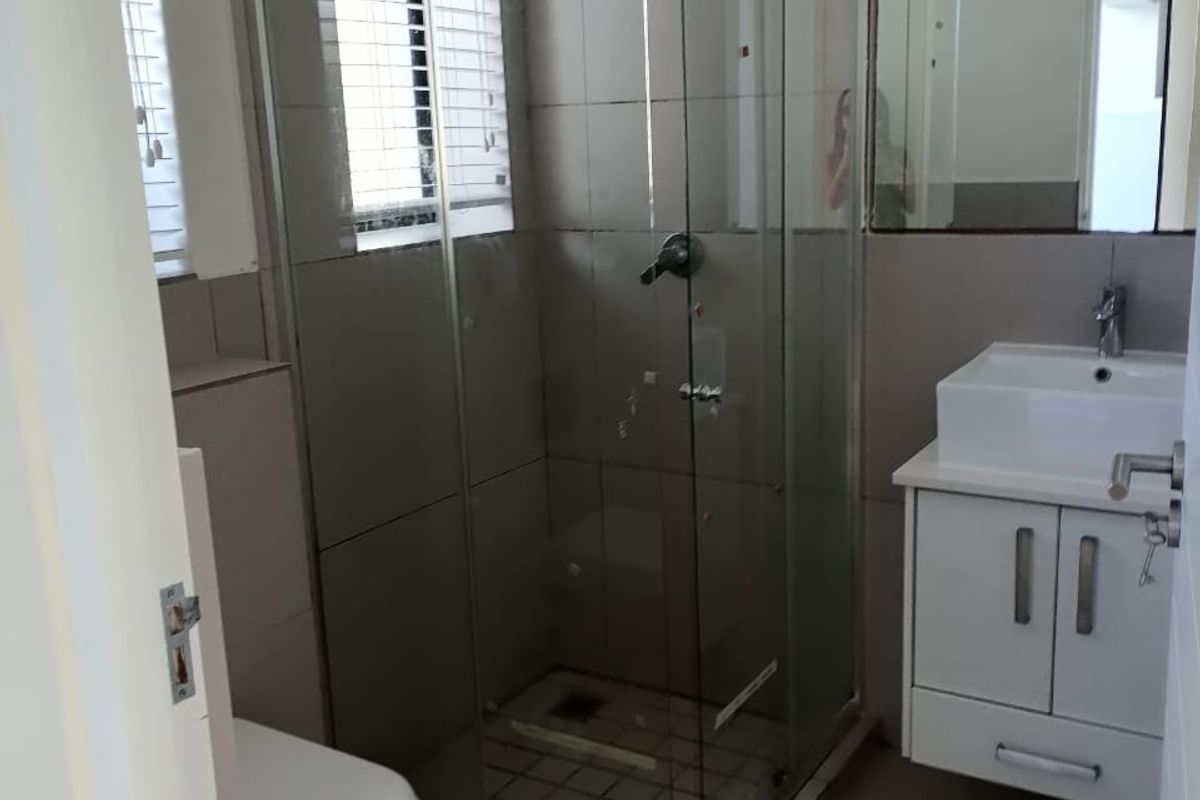 A functional bathroom featuring a glass shower enclosure, wall-mounted vanity with basin, toilet, and neutral tiled finishes throughout.