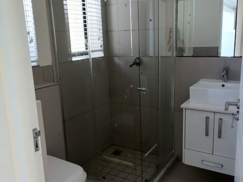 A functional bathroom featuring a glass shower enclosure, wall-mounted vanity with basin, toilet, and neutral tiled finishes throughout.