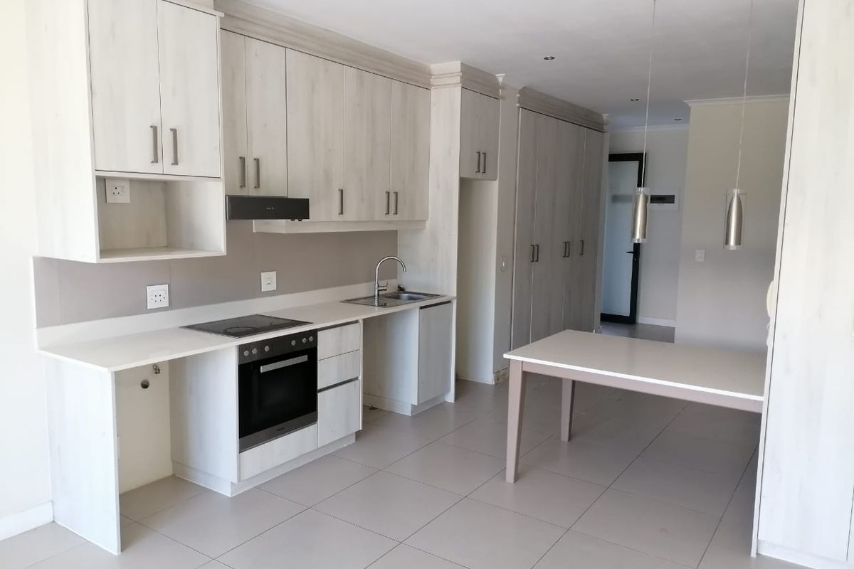 Modern kitchen featuring light wood-finish cabinetry, integrated oven and hob, tiled flooring, and ample storage space in a clean, open-plan layout.
