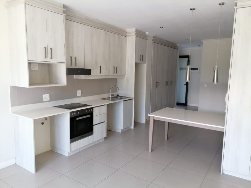 Modern kitchen featuring light wood-finish cabinetry, integrated oven and hob, tiled flooring, and ample storage space in a clean, open-plan layout.