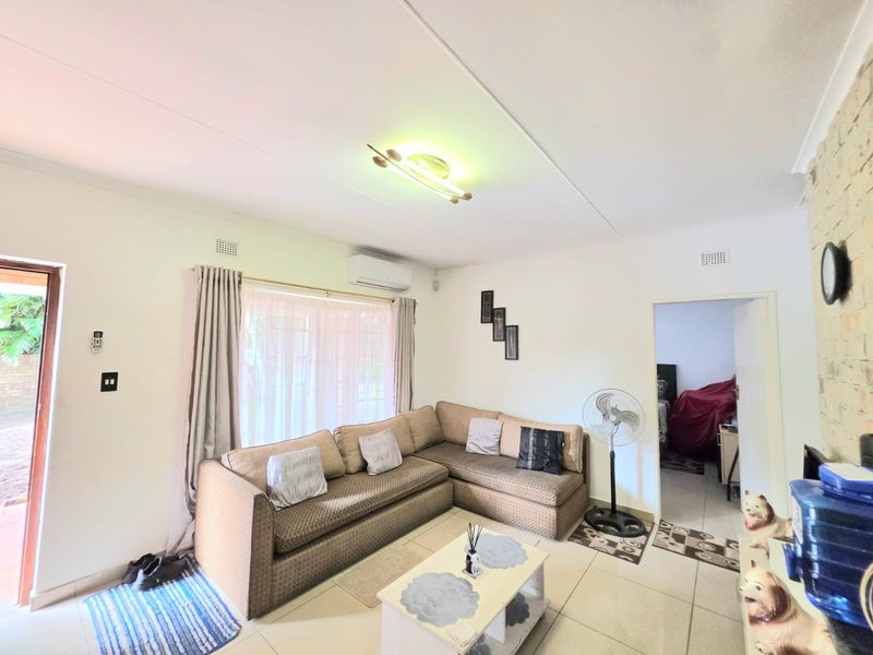 A functional living room featuring tiled flooring, a wall-mounted split-system air conditioner, and direct access to an outdoor area.