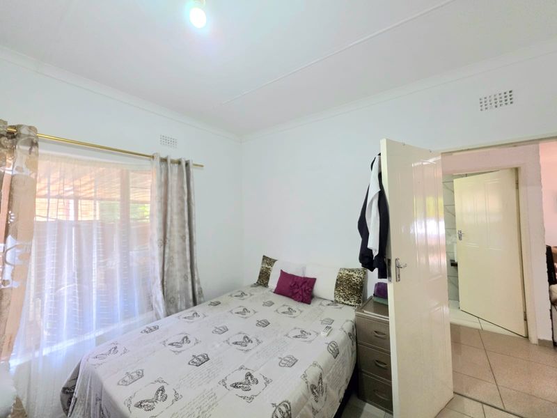 A functional bedroom featuring tiled flooring, neutral walls, and direct access to an adjoining room.