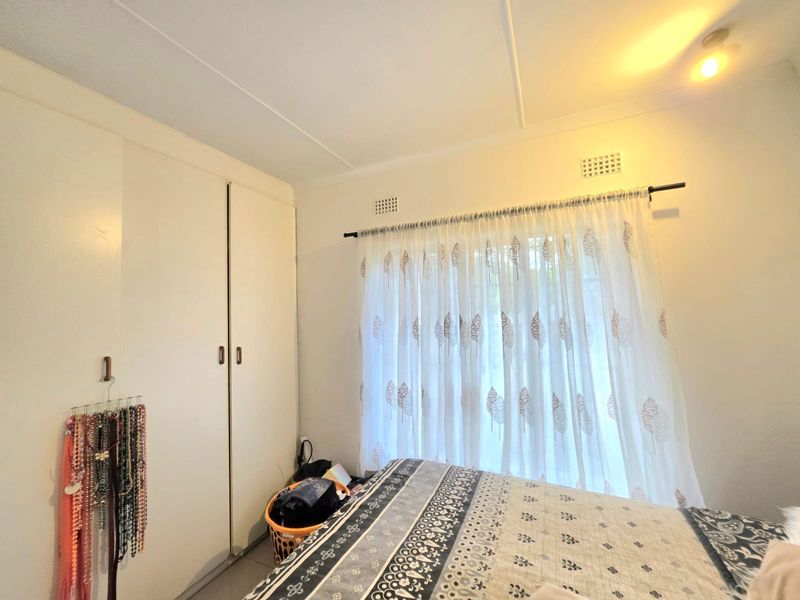 A bedroom featuring built-in cupboards and a window with a curtain rod, providing a functional space with standard finishes.