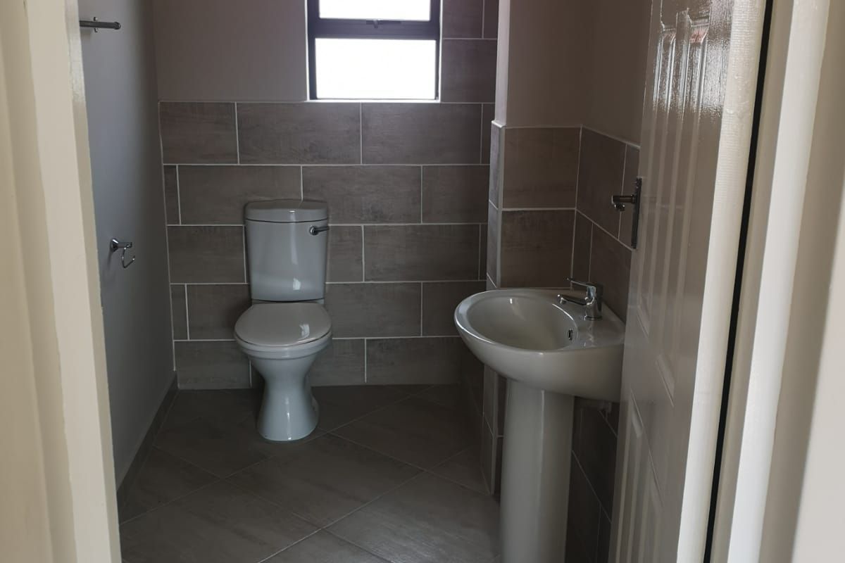 A clean and functional guest bathroom featuring a pedestal basin, toilet, and neutral tiled finishes.