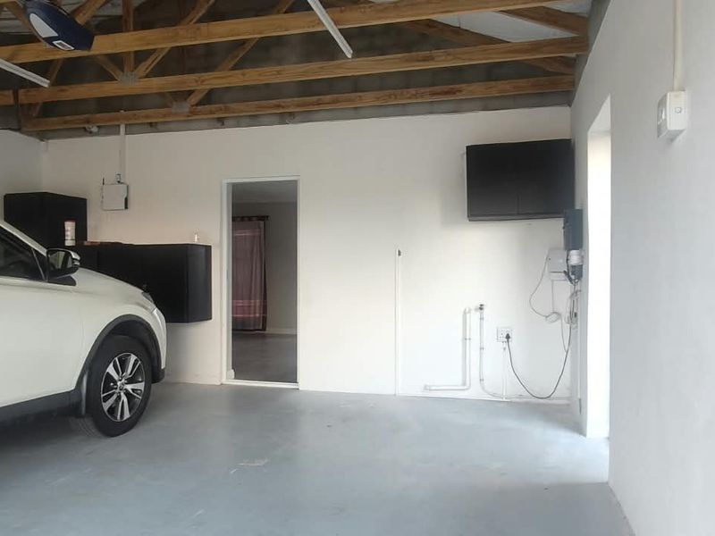 A functional garage space featuring exposed timber roof trusses, concrete flooring, and dedicated plumbing and electrical points for utility use.