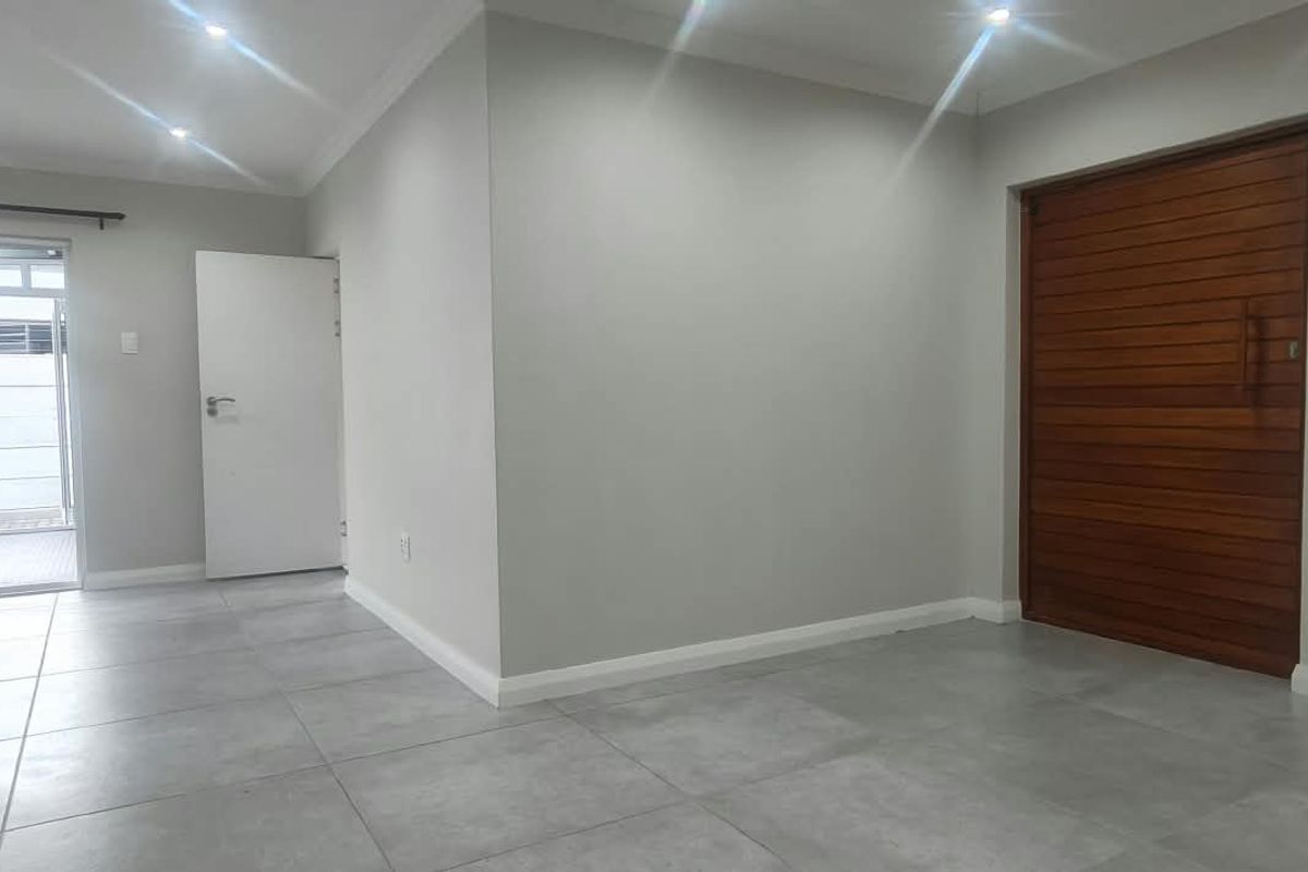 A bright, open-plan living area featuring neutral tiled flooring, recessed downlights, and a distinctive wooden feature door leading to an adjacent space.