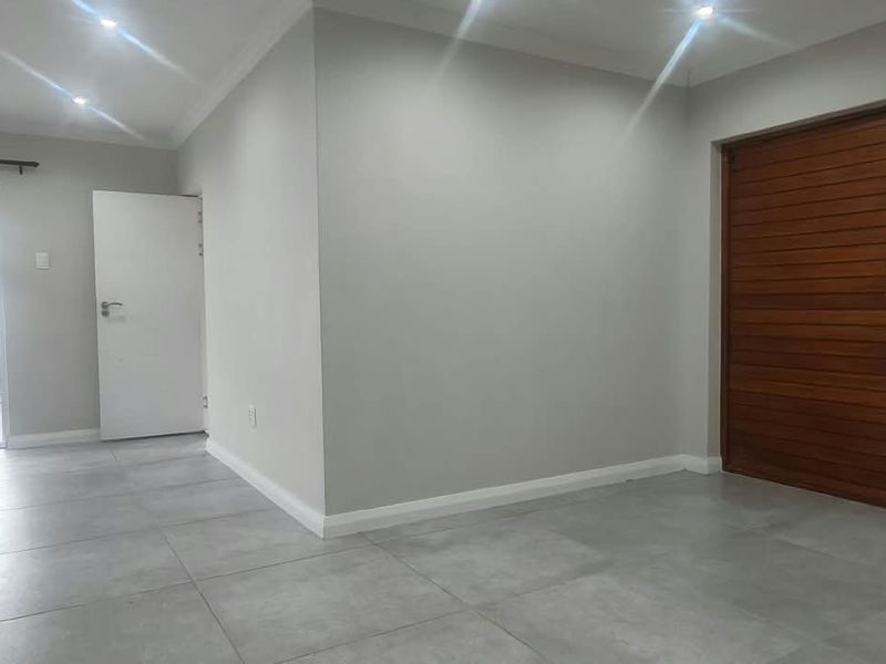 A bright, open-plan living area featuring neutral tiled flooring, recessed downlights, and a distinctive wooden feature door leading to an adjacent space.