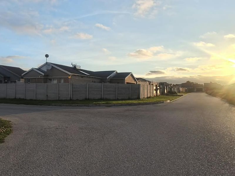 A street-level view of the residential neighbourhood, featuring asphalt roads, concrete boundary walls, and clear views of the surrounding properties at sunset.