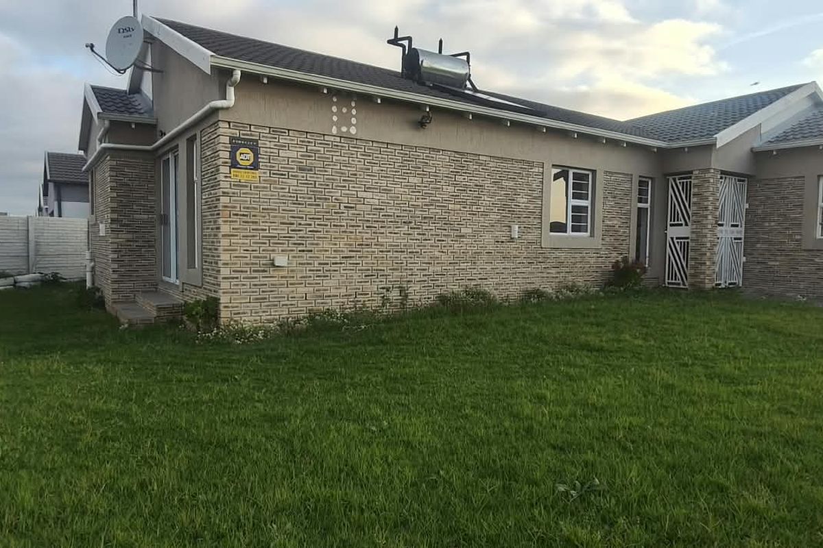 Rear view of a single-story brick house featuring a solar water heater, security gate, and a spacious lawn with a precast concrete boundary wall.