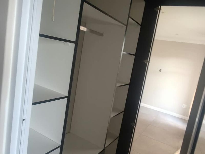 A bedroom featuring built-in wardrobe cabinetry with shelving and hanging space, complemented by neutral tiled flooring and recessed ceiling lighting.