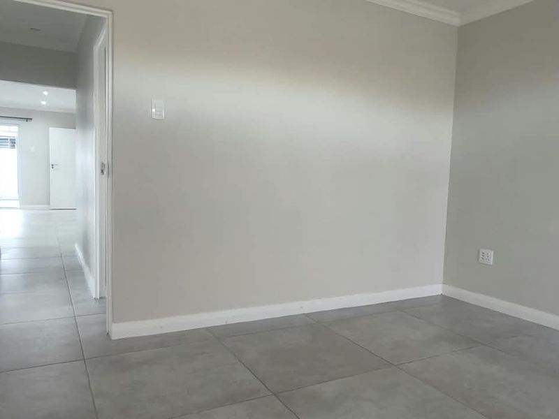 An empty living room featuring neutral grey wall paint and large format floor tiles, leading into a hallway with access to other rooms.