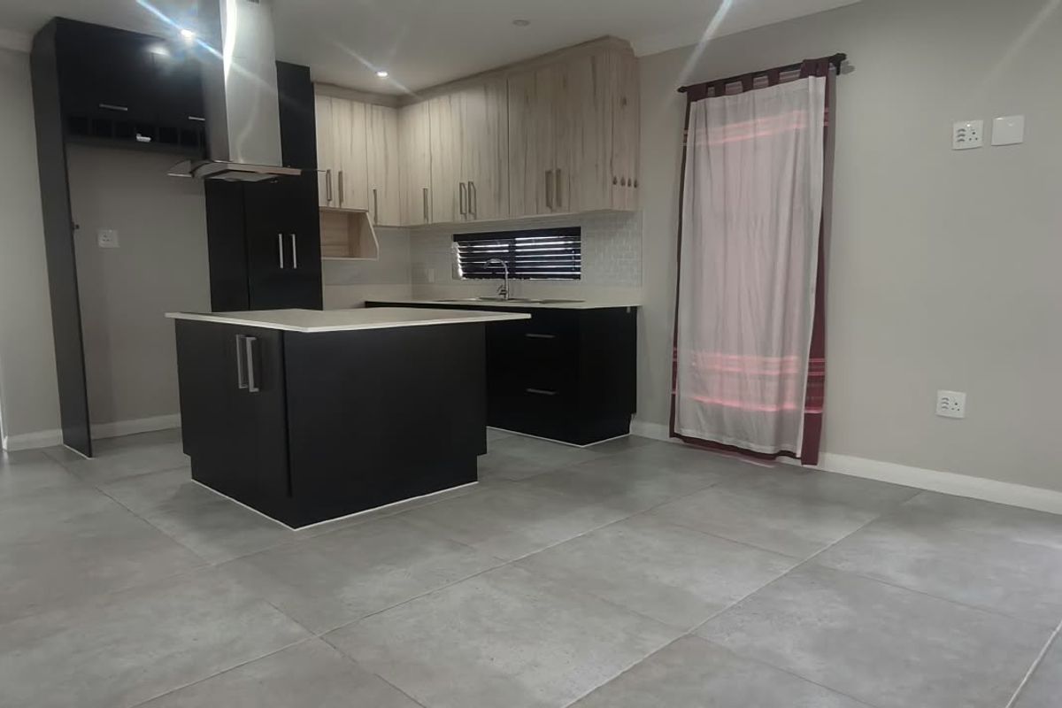 Modern kitchen featuring a central island, sleek two-tone cabinetry, stainless steel extractor fan, and neutral tiled flooring in an open-plan layout.