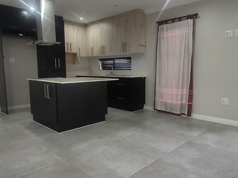 Modern kitchen featuring a central island, sleek two-tone cabinetry, stainless steel extractor fan, and neutral tiled flooring in an open-plan layout.