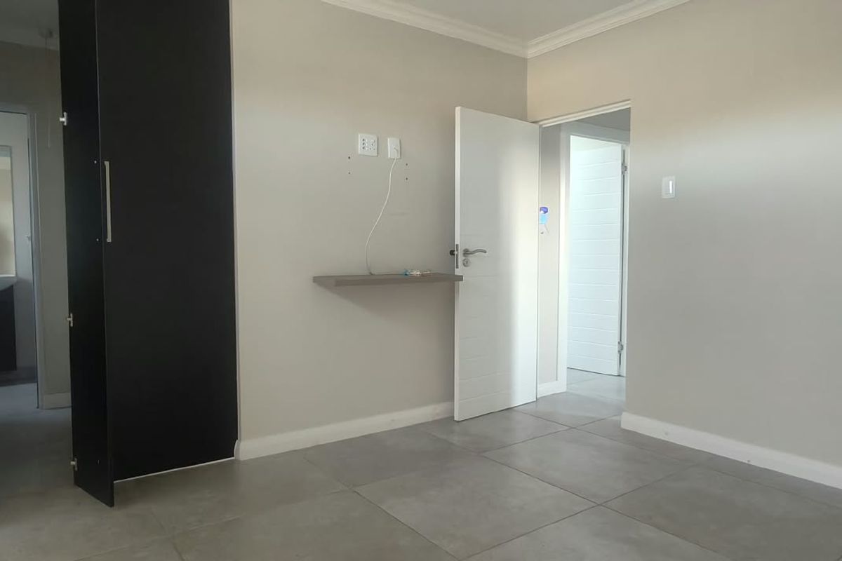 A clean, empty bedroom featuring neutral wall tones, large floor tiles, and a built-in cupboard with an adjacent en-suite bathroom.