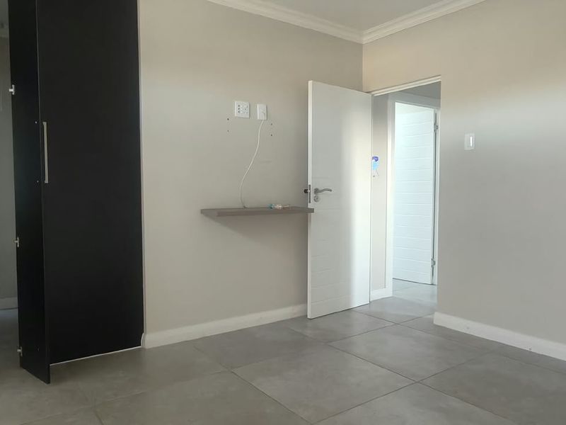 A clean, empty bedroom featuring neutral wall tones, large floor tiles, and a built-in cupboard with an adjacent en-suite bathroom.