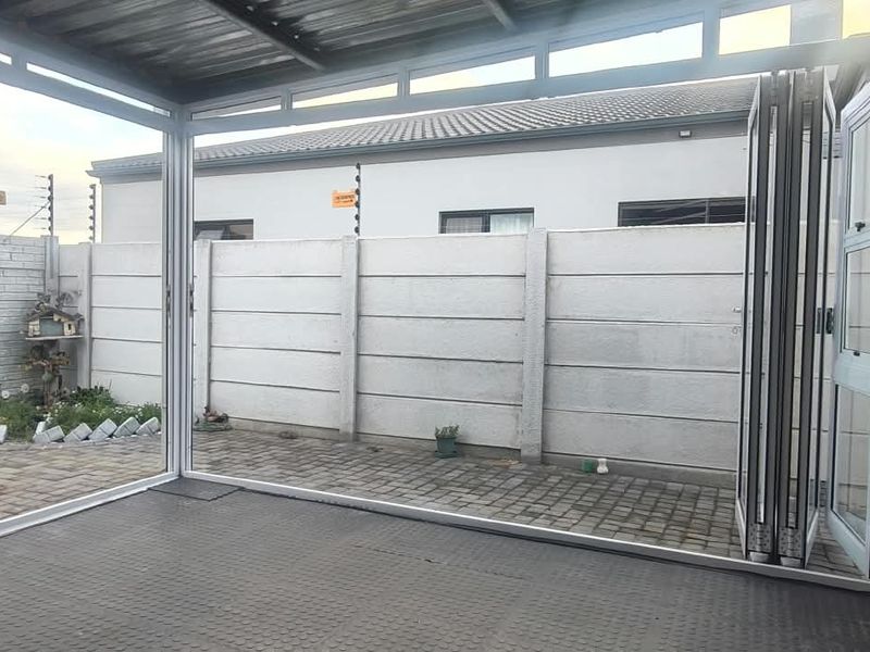 An enclosed patio area featuring a built-in braai, paved flooring, and folding glass doors opening to a private rear garden space.