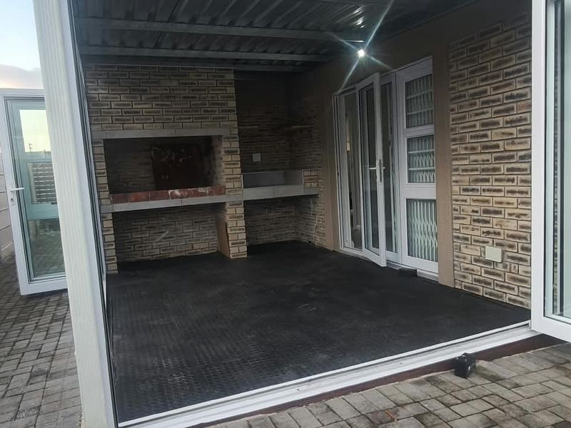 Covered outdoor patio featuring a built-in brick braai, paved flooring, and direct access to the interior through large sliding doors.