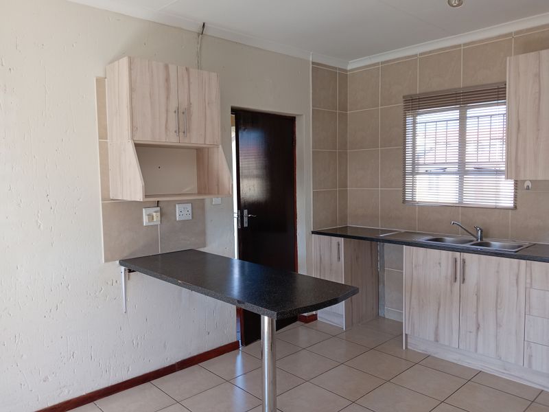 A functional kitchen featuring light wood-look cabinetry, dark laminate countertops, a breakfast bar, and tiled flooring with a neutral tiled splashback.