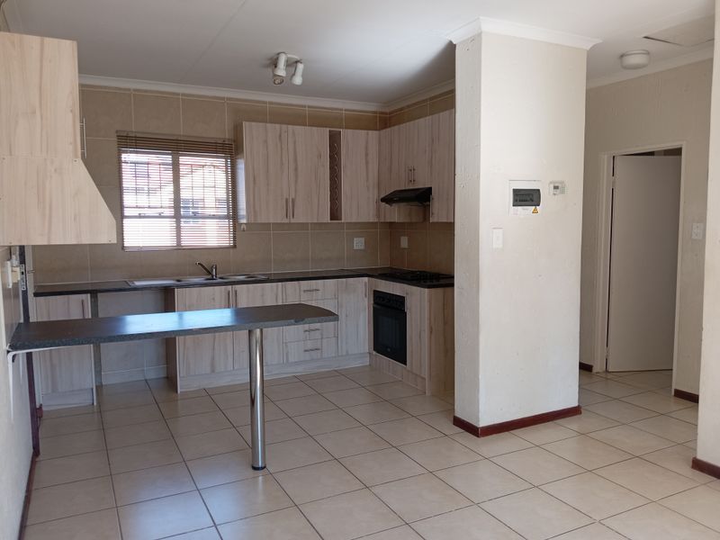 A functional kitchen featuring light wood-finish cabinetry, dark countertops, built-in oven and hob, and tiled flooring, offering a clean and practical workspace.