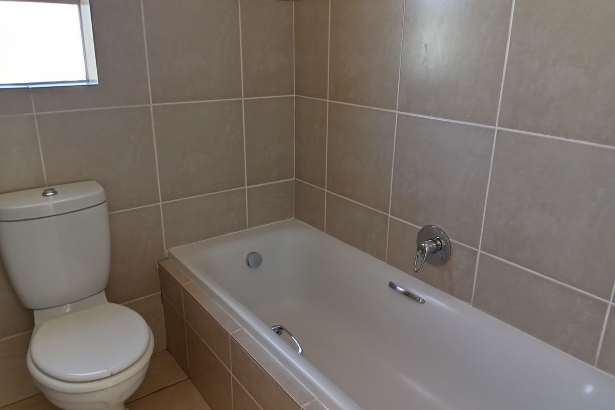 A functional bathroom featuring a built-in bathtub, toilet, and neutral wall and floor tiling.