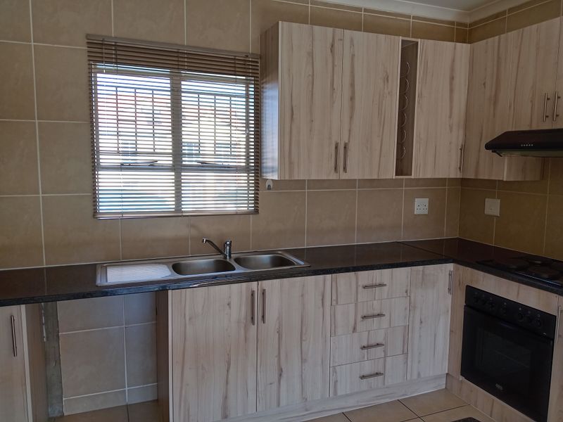 A functional kitchen featuring light wood-grain cabinetry, dark laminate countertops, a double sink, and integrated oven and hob with a tiled splashback.