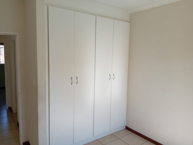 A clean, empty bedroom featuring neutral walls, tiled flooring, and white built-in cupboards providing ample storage space.