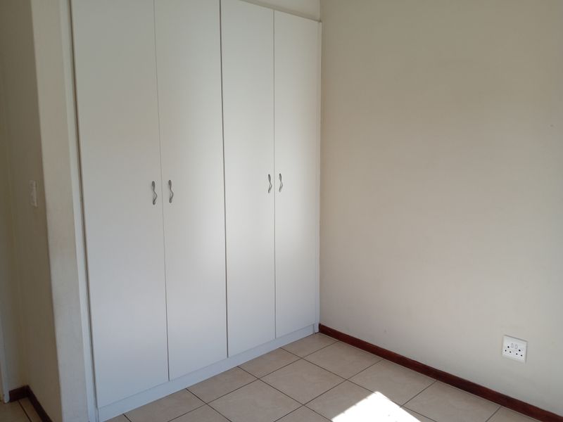 A clean, empty bedroom featuring neutral tiled flooring and white built-in cupboards, providing a versatile space ready for personalization.