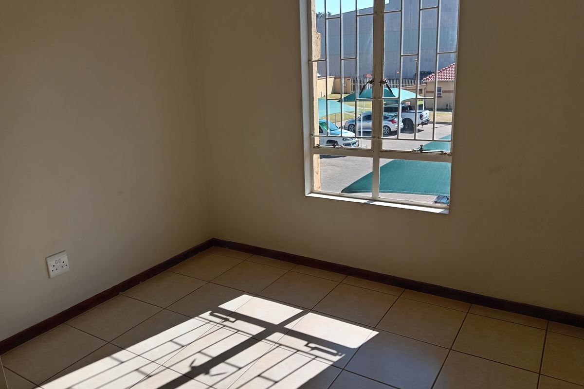 An empty bedroom featuring neutral tiled flooring, security bars on the window, and standard electrical fixtures, ready for personalization.