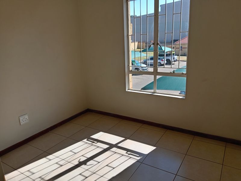 An empty bedroom featuring neutral tiled flooring, security bars on the window, and standard electrical fixtures, ready for personalization.