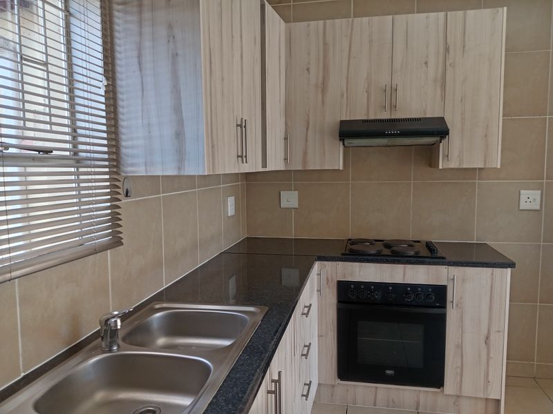 A clean, functional kitchen featuring light wood-finish cabinetry, granite countertops, a double sink, and built-in oven with hob and extractor fan.