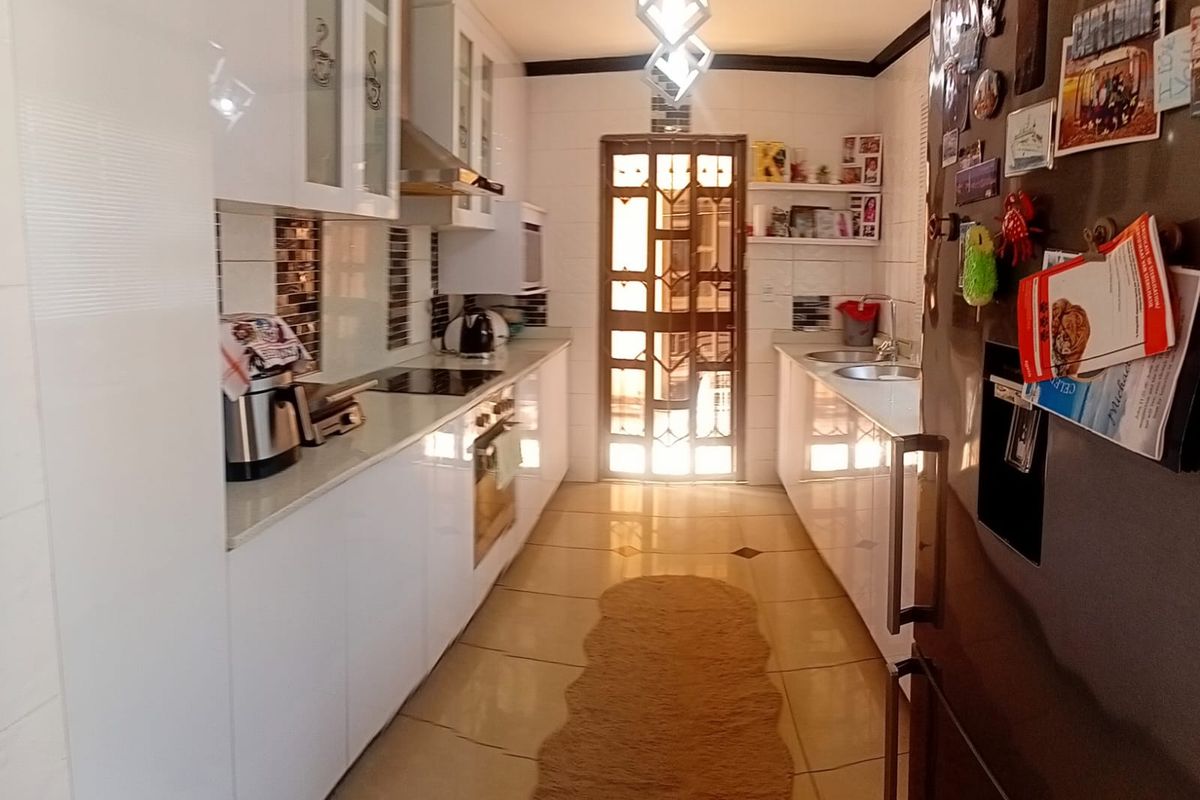 A functional galley-style kitchen featuring white cabinetry, integrated appliances, tiled flooring, and a secure rear exit door.