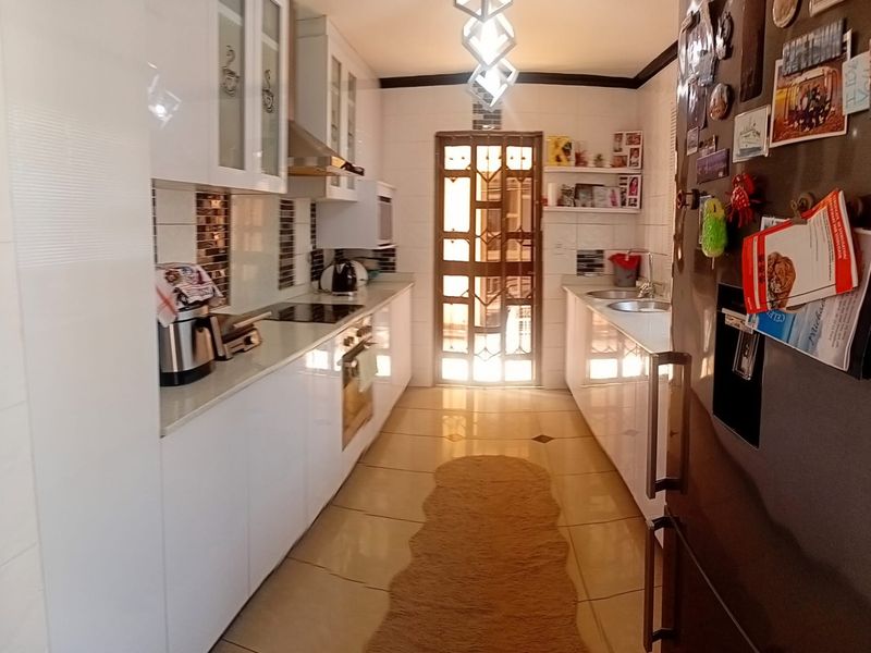 A functional galley-style kitchen featuring white cabinetry, integrated appliances, tiled flooring, and a secure rear exit door.