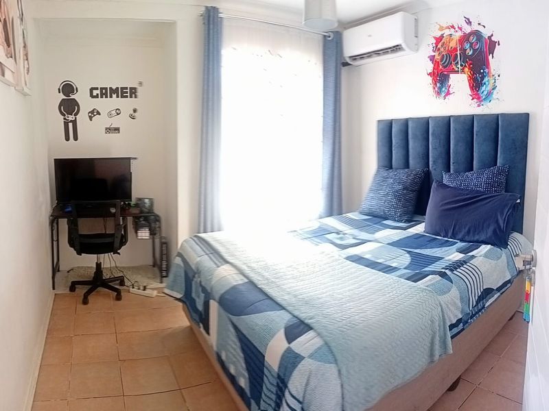 A functional bedroom featuring tiled flooring and a wall-mounted split-system air conditioner, providing a comfortable and climate-controlled living space.