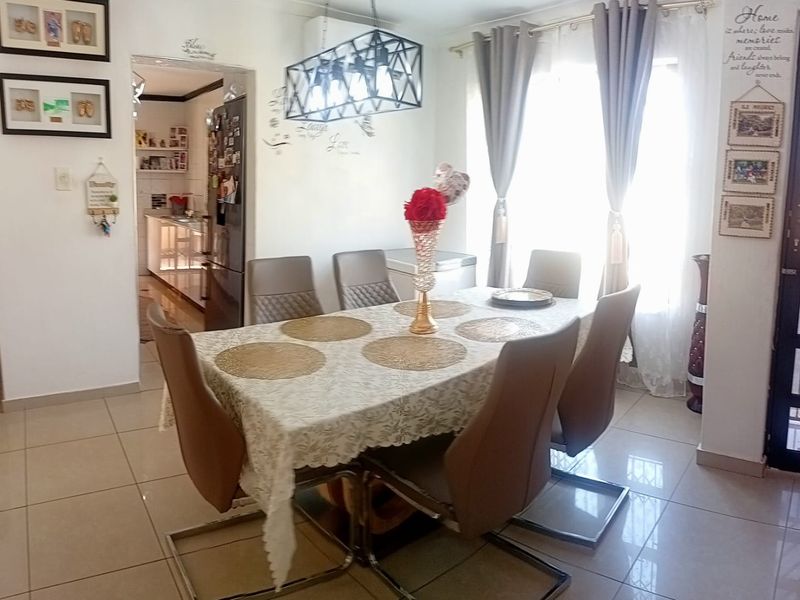 A well-lit dining room featuring tiled flooring and a modern pendant light fixture, with an open-plan flow leading into the adjacent kitchen area.