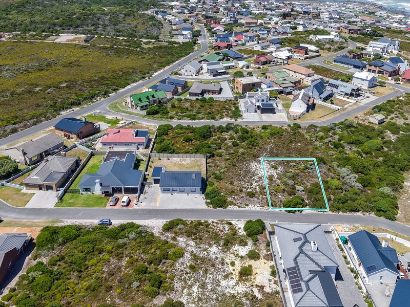 Aerial view of a vacant residential plot situated in a developed coastal neighborhood with established road access and surrounding homes.