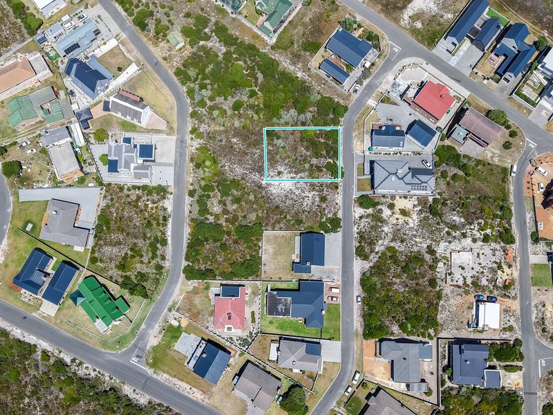 An aerial view of a vacant residential plot situated within an established coastal neighborhood, highlighting the surrounding infrastructure and local landscape.