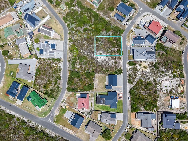 An aerial view of a vacant residential plot situated within a developed coastal neighborhood, highlighting the surrounding infrastructure and natural vegetation.